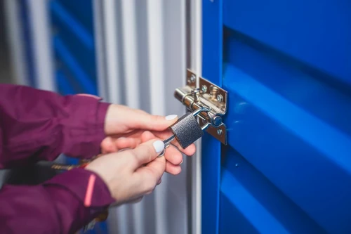 A person locking a blue self storage unit with a padlock